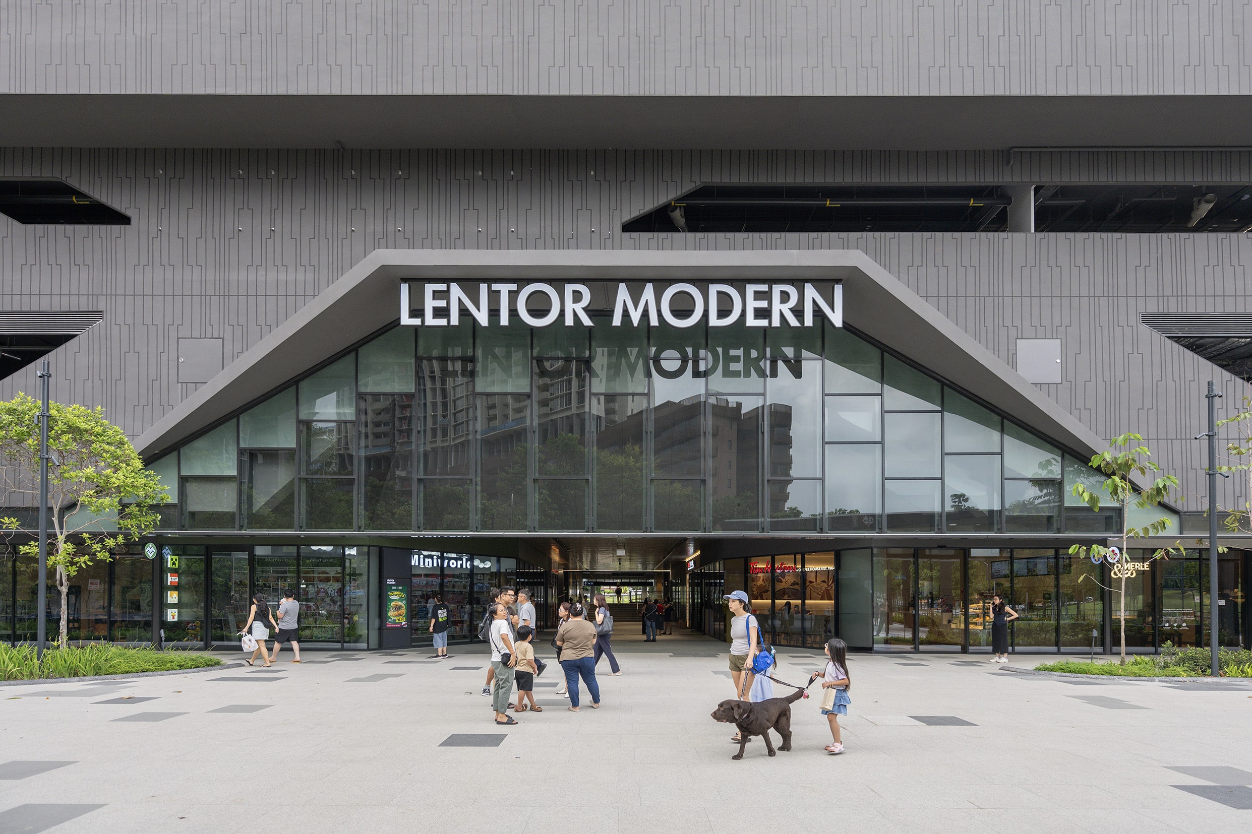 Exterior facade of Lentor Modern mall at Lentor MRT station with shoppers and families walking outside the modern architectural entrance
