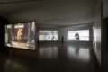 Multi-channel video installation by Young-jun Tak featuring suspended screens projecting both colour and black-and-white footage in a dimly lit gallery at Taipei Biennial 2025.