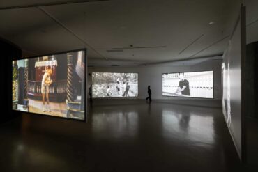 Multi-channel video installation by Young-jun Tak featuring suspended screens projecting both colour and black-and-white footage in a dimly lit gallery at Taipei Biennial 2025.