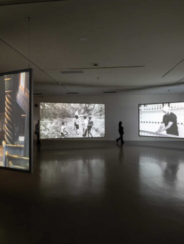 Multi-channel video installation by Young-jun Tak featuring suspended screens projecting both colour and black-and-white footage in a dimly lit gallery at Taipei Biennial 2025.