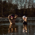 Man and woman practising ice bath cold water immersion together in a frozen lake, highlighting the mental and physical benefits of cold exposure in nature.