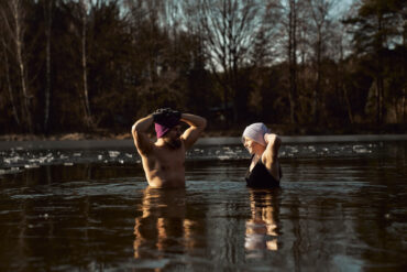 Man and woman practising ice bath cold water immersion together in a frozen lake, highlighting the mental and physical benefits of cold exposure in nature.