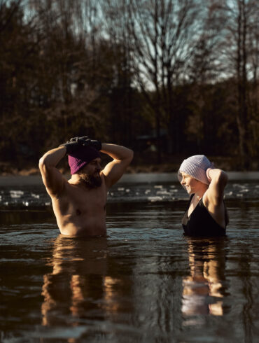 Man and woman practising ice bath cold water immersion together in a frozen lake, highlighting the mental and physical benefits of cold exposure in nature.