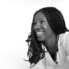 Profile photo of African woman with long hair wearing a white blouse.