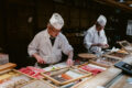 Japanese sushi chefs in traditional white uniforms preparing fresh fish at a sushi counter with wooden trays of tuna, salmon, and seafood for new restaurants in Singapore