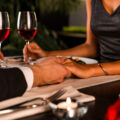Couple holding hands over candlelit dinner table with red wine for Valentine’s Day celebration in Singapore 2026.