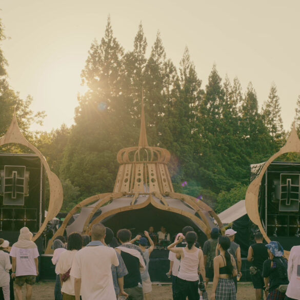 Golden hour at rural 2026 main stage with warm sunset glow and deep listening crowd immersed in techno, set against the forests of Fukushima, Japan