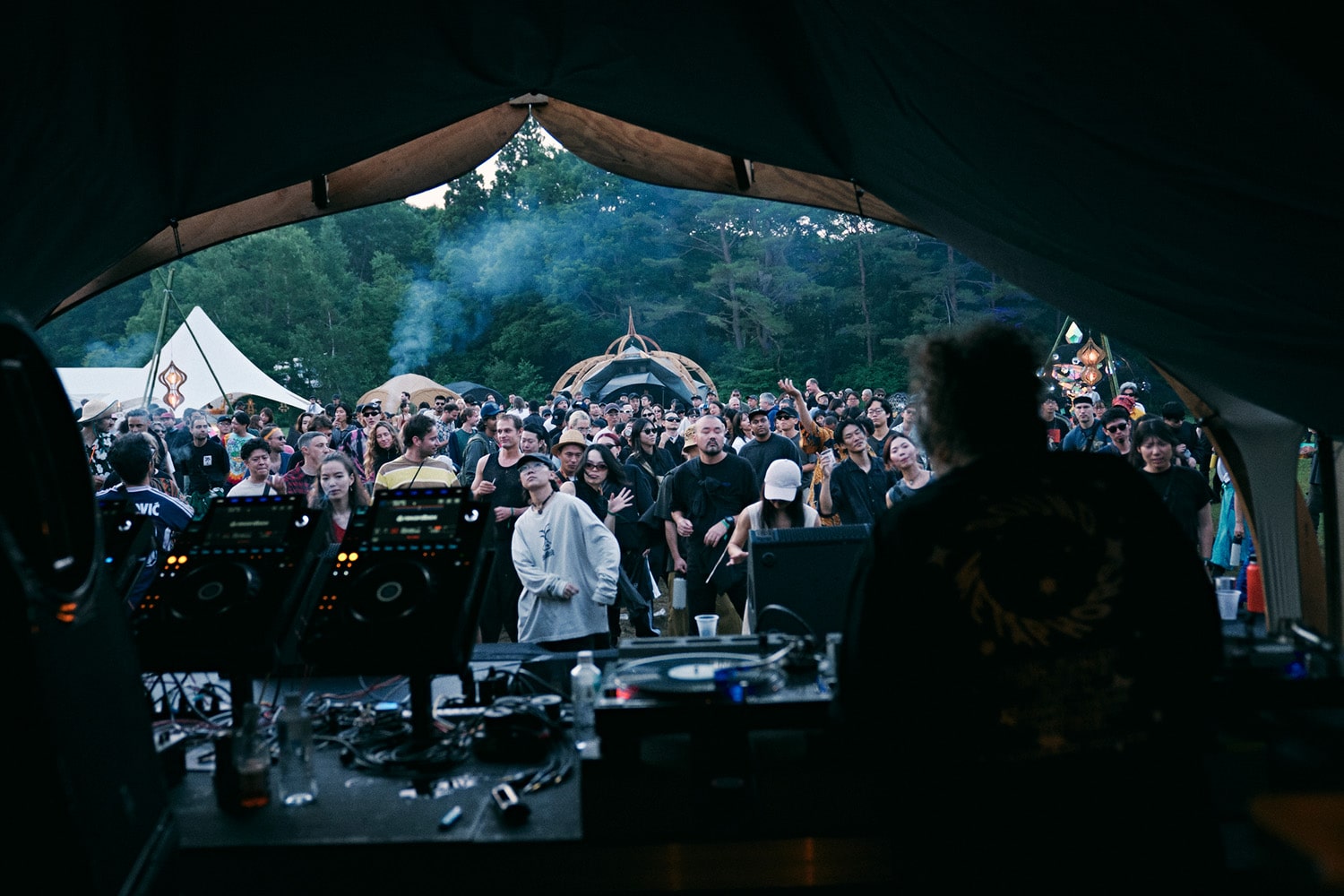 DJ perspective of dancing crowd at rural techno festival in Fukushima, Japan, highlighting community energy and outdoor forest setting