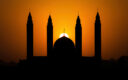 Silhouette of mosque dome and minarets against an orange sunset sky during Ramadan.