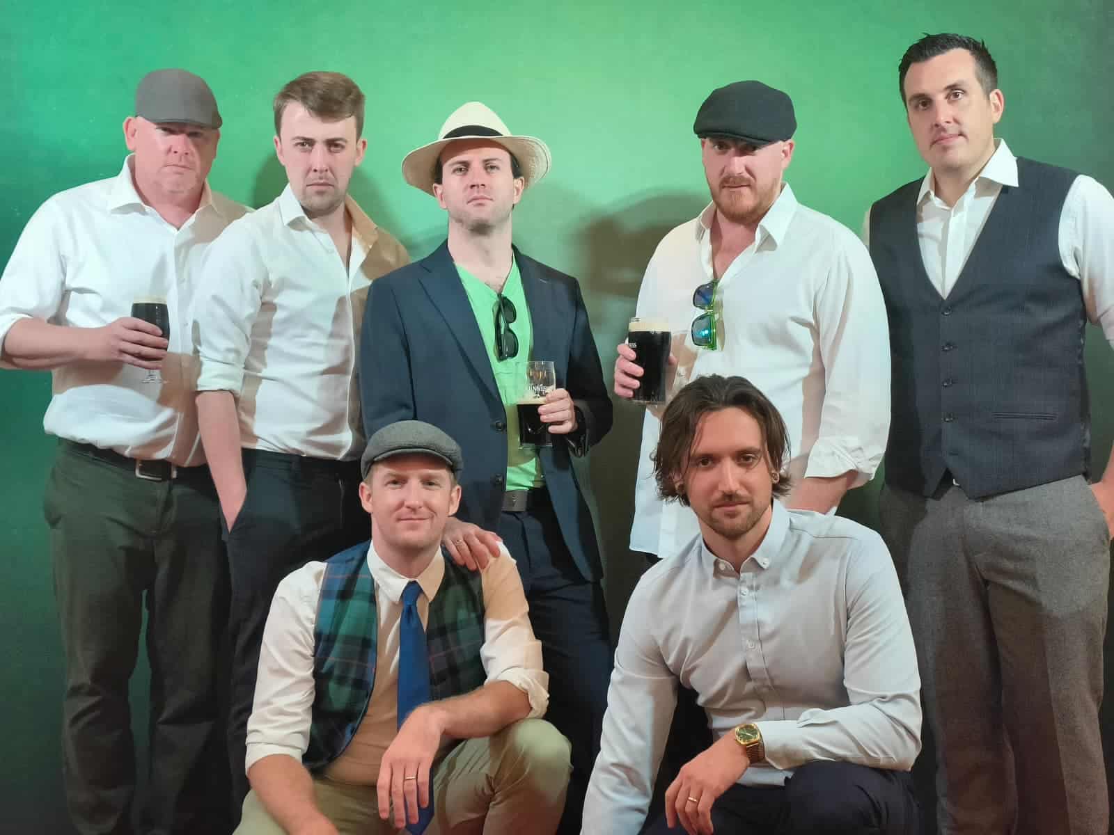 Celtic rock band Gan Ainm posing together with pints of Guinness against a green backdrop.