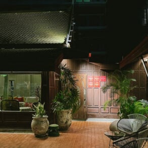 Night view of Gaa Bangkok’s courtyard with traditional wooden architecture and lush greenery.