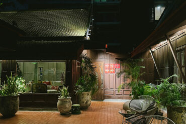 Night view of Gaa Bangkok’s courtyard with traditional wooden architecture and lush greenery.