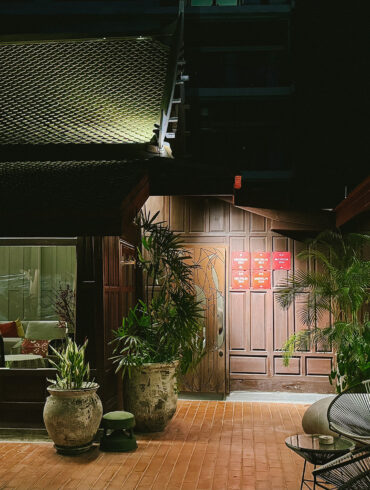 Night view of Gaa Bangkok’s courtyard with traditional wooden architecture and lush greenery.