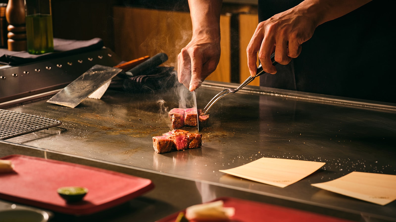 Chef slicing seared wagyu beef on a teppanyaki grill at Nobu Singapore during a live cooking demonstration.