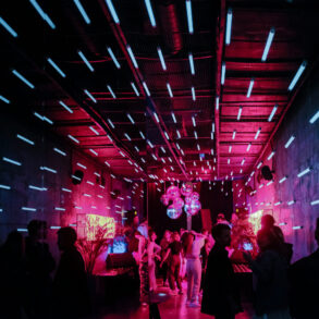 Crowd dancing under neon pink and blue lights inside an underground electronic music club in Moscow, Russia.