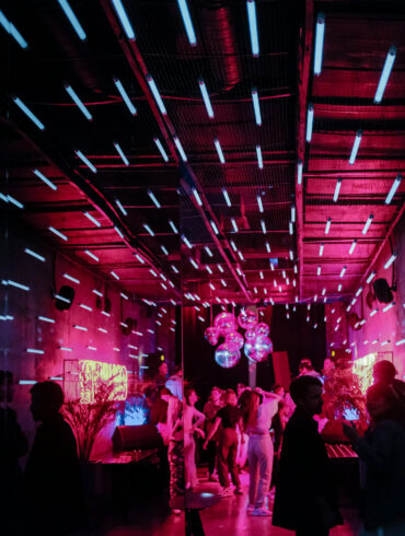 Crowd dancing under neon pink and blue lights inside an underground electronic music club in Moscow, Russia.