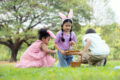 Children wearing bunny ears searching for Easter eggs in a park, holding baskets during an outdoor Easter egg hunt.