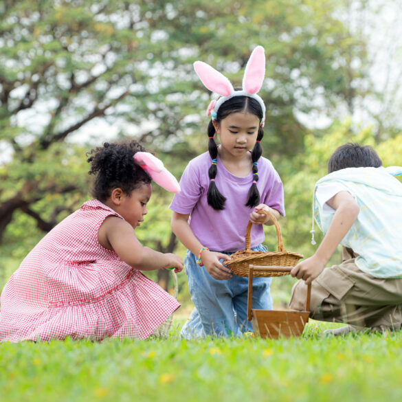 Children wearing bunny ears searching for Easter eggs in a park, holding baskets during an outdoor Easter egg hunt.