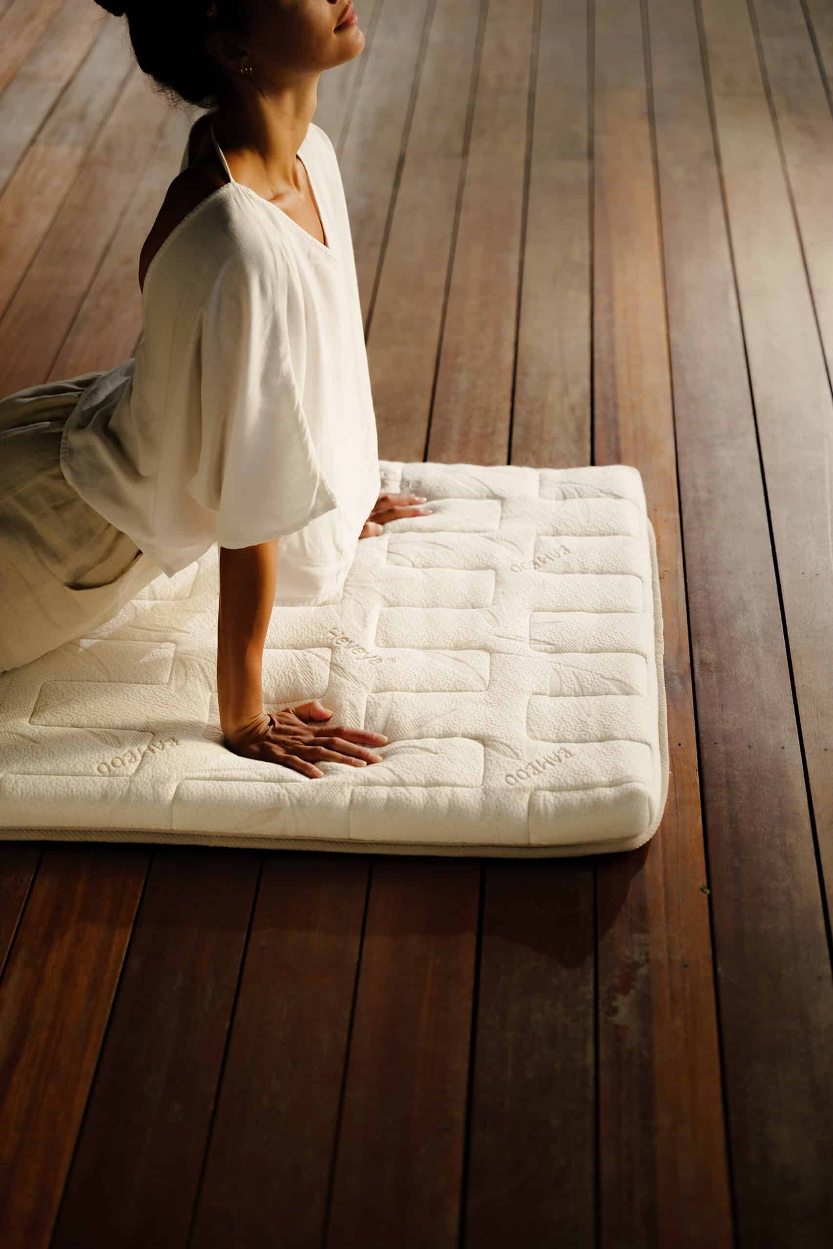Person practicing a yoga stretch on a natural latex meditation mat on a wooden deck.