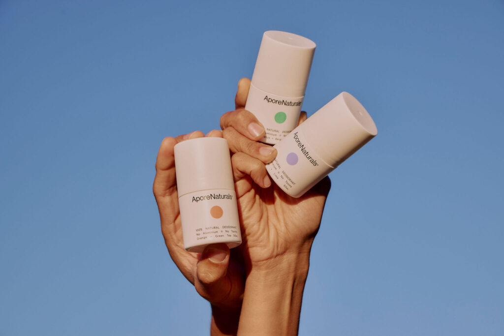 Three AporeNaturals natural roll-on deodorants held up against a blue sky in Singapore