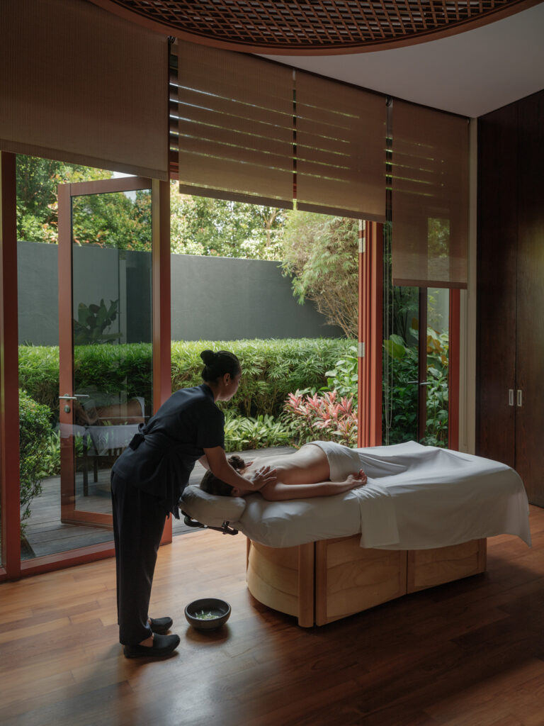 A therapist performing a massage in a treatment room at Auriga Spa, Capella Singapore, overlooking lush greenery