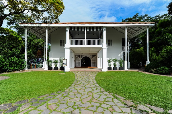 The white colonial façade of Burkill Hall at Singapore Botanic Gardens, framed by lush greenery and a stone pathway