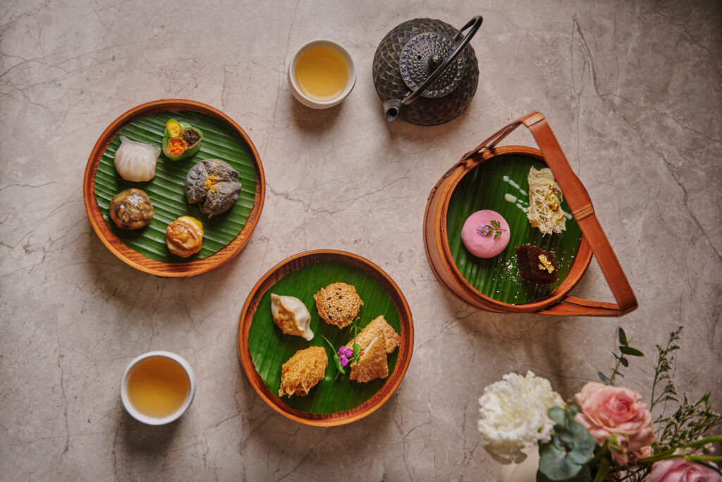 Overhead shot of Cassia's Oriental Dim Sum Afternoon Tea, featuring bamboo steamer baskets of handcrafted dim sum, tea and flowers at Capella Singapore