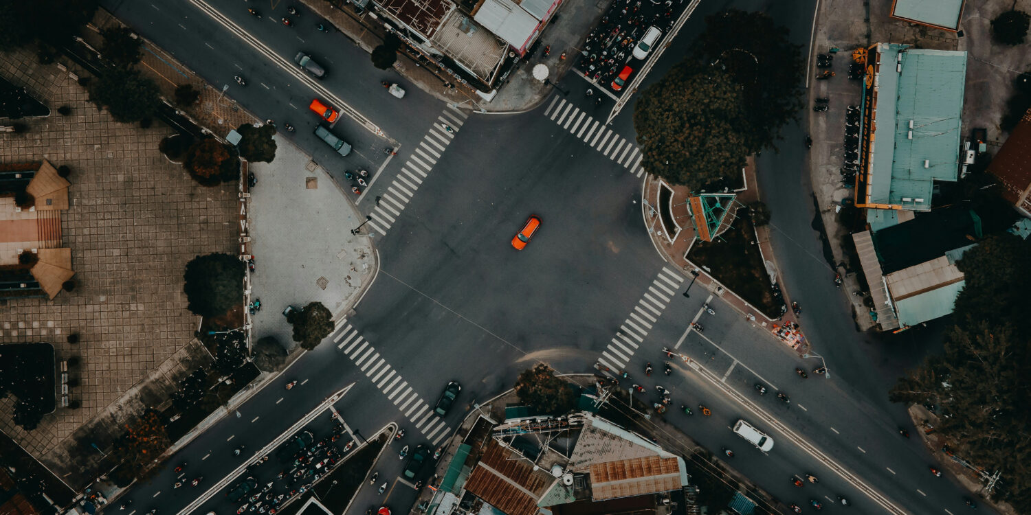 A top view photo of a road unction with motorcycles and cars waiting in traffic lights and an orange car crossing it in Ho Chi Minh Vietnam
