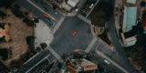A top view photo of a road unction with motorcycles and cars waiting in traffic lights and an orange car crossing it in Ho Chi Minh Vietnam