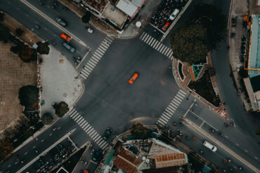 A top view photo of a road unction with motorcycles and cars waiting in traffic lights and an orange car crossing it in Ho Chi Minh Vietnam