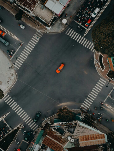 A top view photo of a road unction with motorcycles and cars waiting in traffic lights and an orange car crossing it in Ho Chi Minh Vietnam