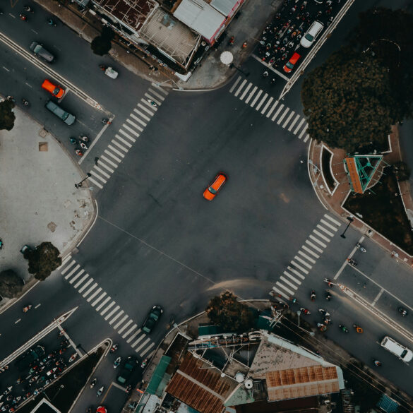 A top view photo of a road unction with motorcycles and cars waiting in traffic lights and an orange car crossing it in Ho Chi Minh Vietnam