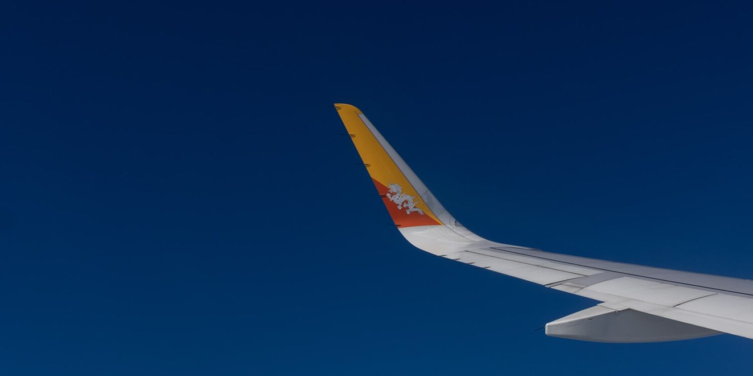 Drukair aircraft wing with Bhutan’s dragon emblem flying against a clear blue sky
