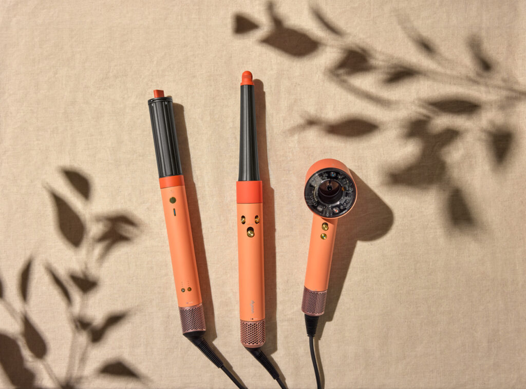 Dyson Ceramic Apricot and Topaz limited-edition hair care devices laid flat on a neutral linen background