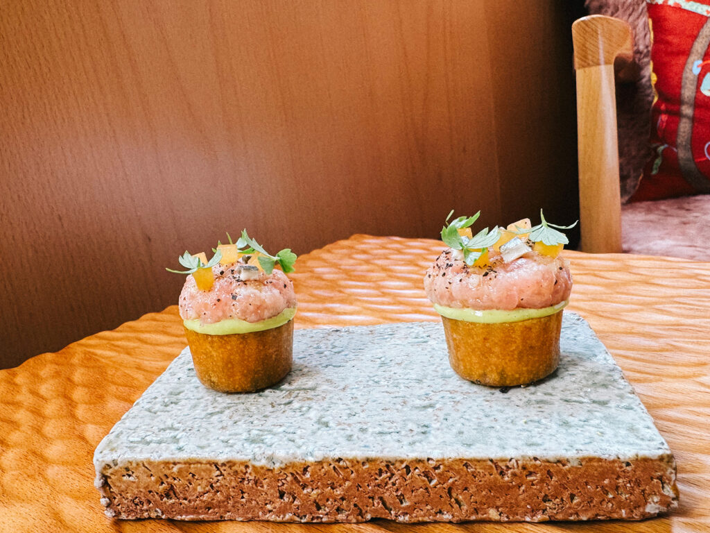 Two canapé tartlets filled with amberjack and topped with microgreens and diced citrus, served on a textured stone slab at Zén restaurant Singapore.