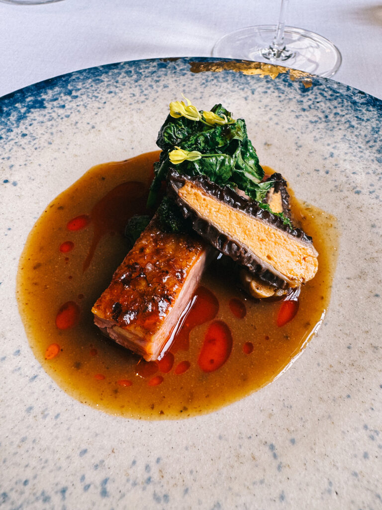 The Guinea Fowl course at Zén, plated on a speckled blue-rimmed ceramic dish with a glazed piece of meat, a slice of foie gras, wilted greens and a rich jus dotted with red chilli oil.