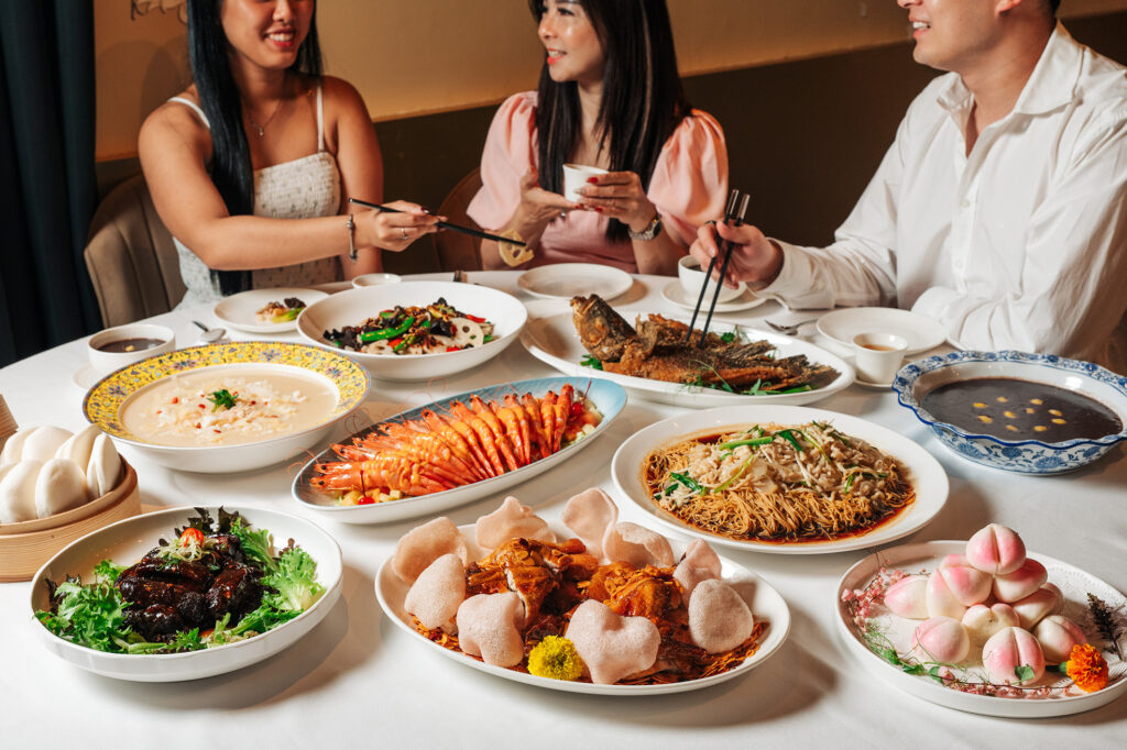 Three diners sharing a feast of Cantonese and Teochew dishes including tiger prawns, noodles, longevity buns and braised meats at MIMI, The Riverhouse Singapore