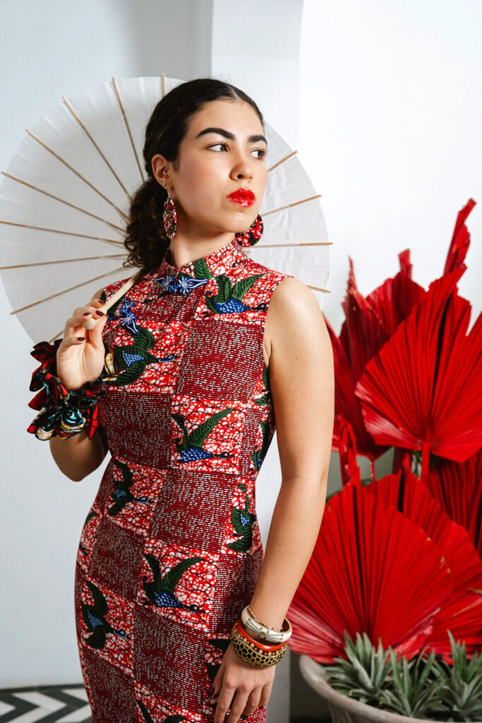 A model wearing an OliveAnkara cheongsam dress in a bold red and green African wax print, styled with matching earrings