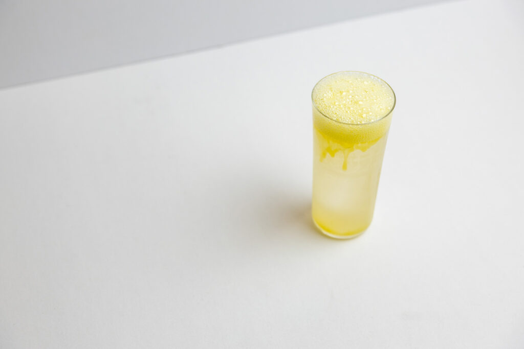 A tall glass of the Pandan x Coconut cocktail, clarified and topped with micro-bubbles, against a white background at Players Table, Singapore.