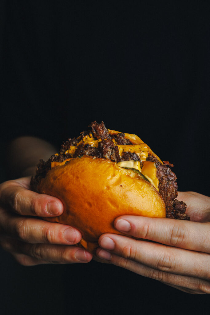  Two hands holding a Classic Smash Burger from Smash Street, showing crispy caramelised patties, melted cheese and house sauce on a toasted potato bun, Amoy Street, Singapore.
