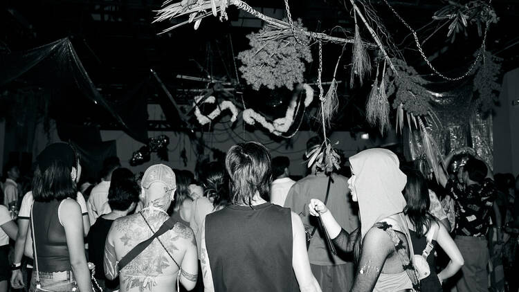 Crowd gathered in a dimly lit underground party space with hanging installations and experimental setup