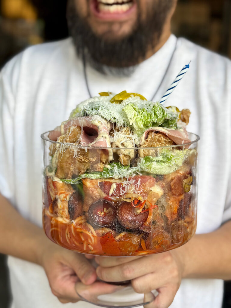  Chef Bjorn Shen holding the Super Bowl Supreme, an oversized glass bowl layered with pepperoni pizza, meatball spaghetti, mortadella, Caesar salad and fried chicken, at Artichoke Pizza Parlor, New Bahru, Singapo