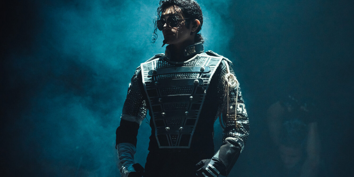 Performer dressed as Michael Jackson in a futuristic stage costume, standing under dramatic blue lighting during a live tribute show.