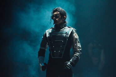 Performer dressed as Michael Jackson in a futuristic stage costume, standing under dramatic blue lighting during a live tribute show.