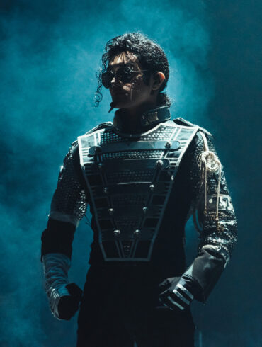 Performer dressed as Michael Jackson in a futuristic stage costume, standing under dramatic blue lighting during a live tribute show.