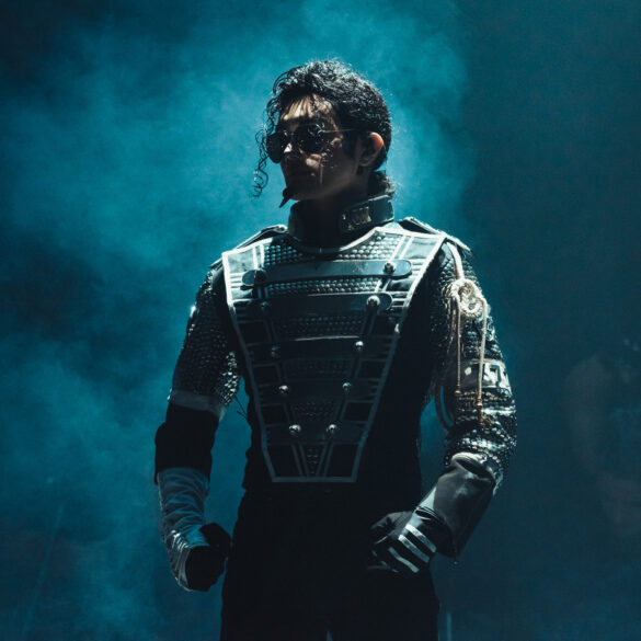 Performer dressed as Michael Jackson in a futuristic stage costume, standing under dramatic blue lighting during a live tribute show.