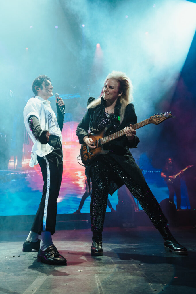 Michael Jackson tribute performer singing alongside a live guitarist on stage, surrounded by atmospheric lighting and concert effects.