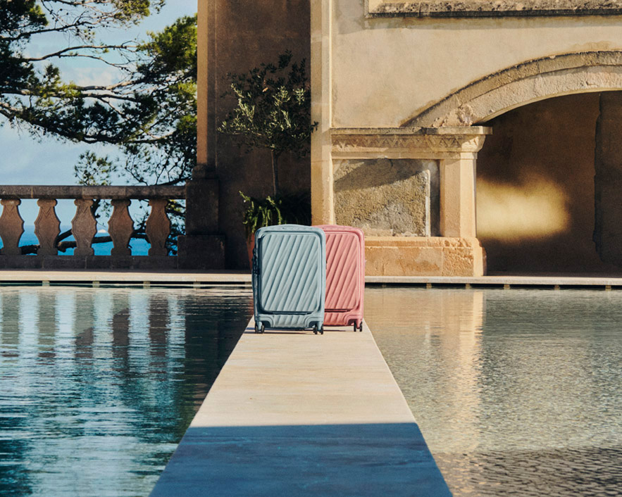 Two TUMI 19 Degree Front Access luggage pieces in Thyme and Pink Clay by a Mediterranean poolside