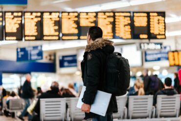 A male traveller holding a laptop looks at a flight information board at an airport terminal.