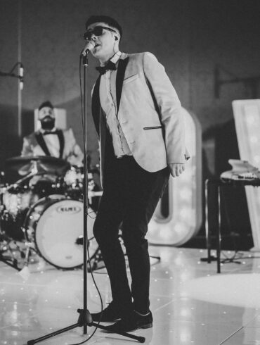 Wedding live band performing on stage with singer and musicians in formal attire, entertaining guests at a reception with illuminated ‘LOVE’ letters.